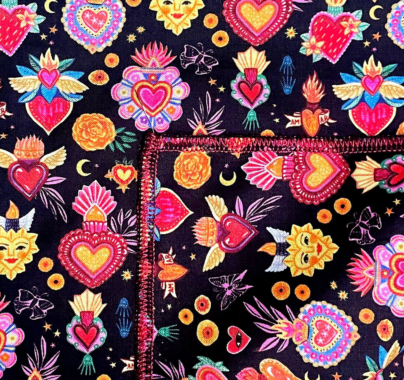 Sacred hearts, suns, moons, flames, wings, butterflies are all small images which cover this fabric. We have made it into a square bandana approx. 21.5" x 21.5" the fabric is machine washable 100% cotton
